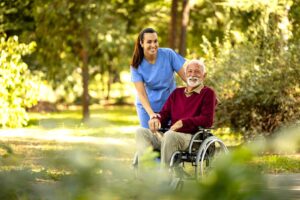 Older adult sits with a small dog in a bright assisted living apartment beside a leash and pet bowls.